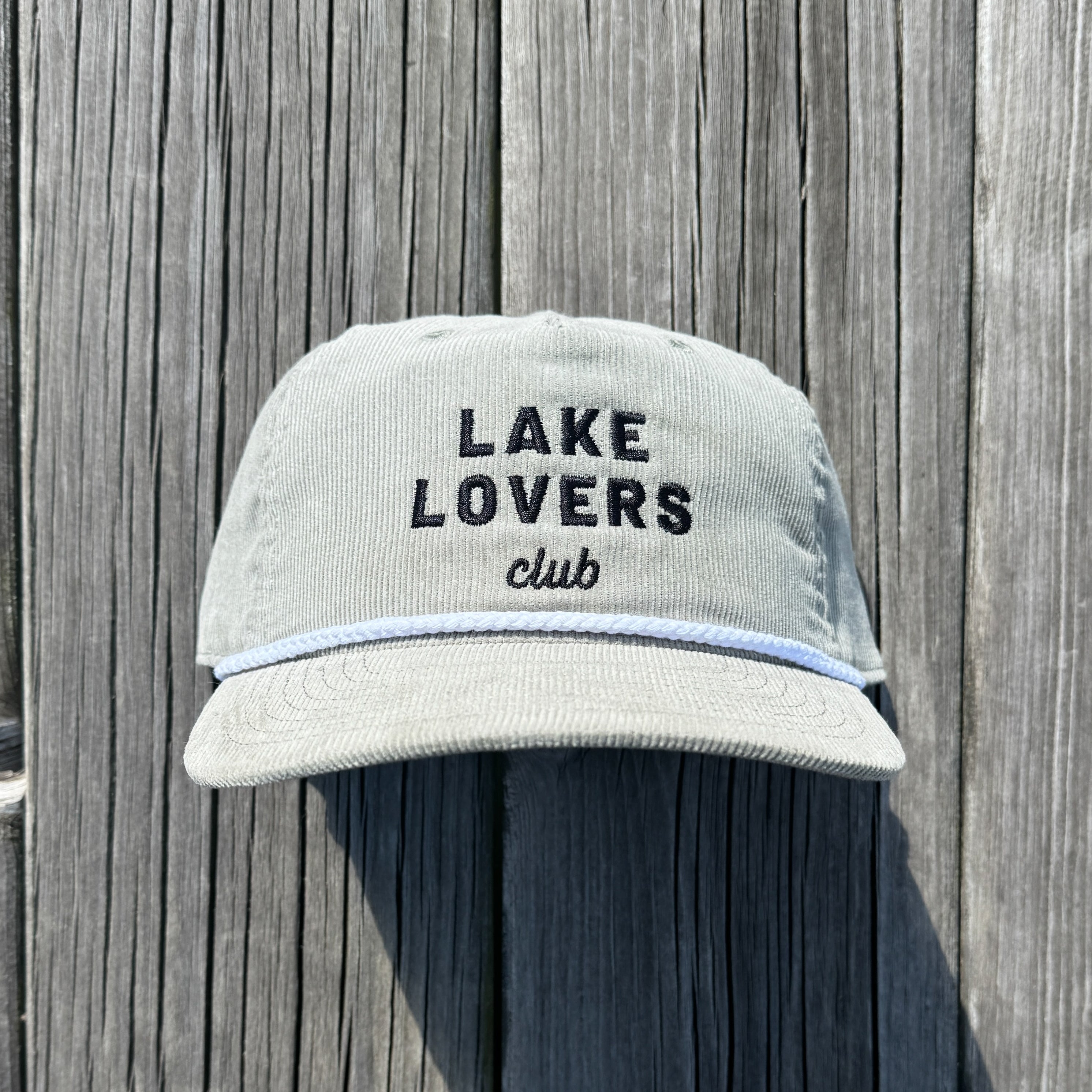 Beige cap with 'Lake Lovers club' text on a wooden background.